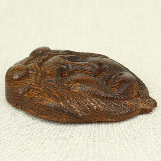 Treen - a carved oak fragment or furniture embellishment, carved as a mask with glass eyes