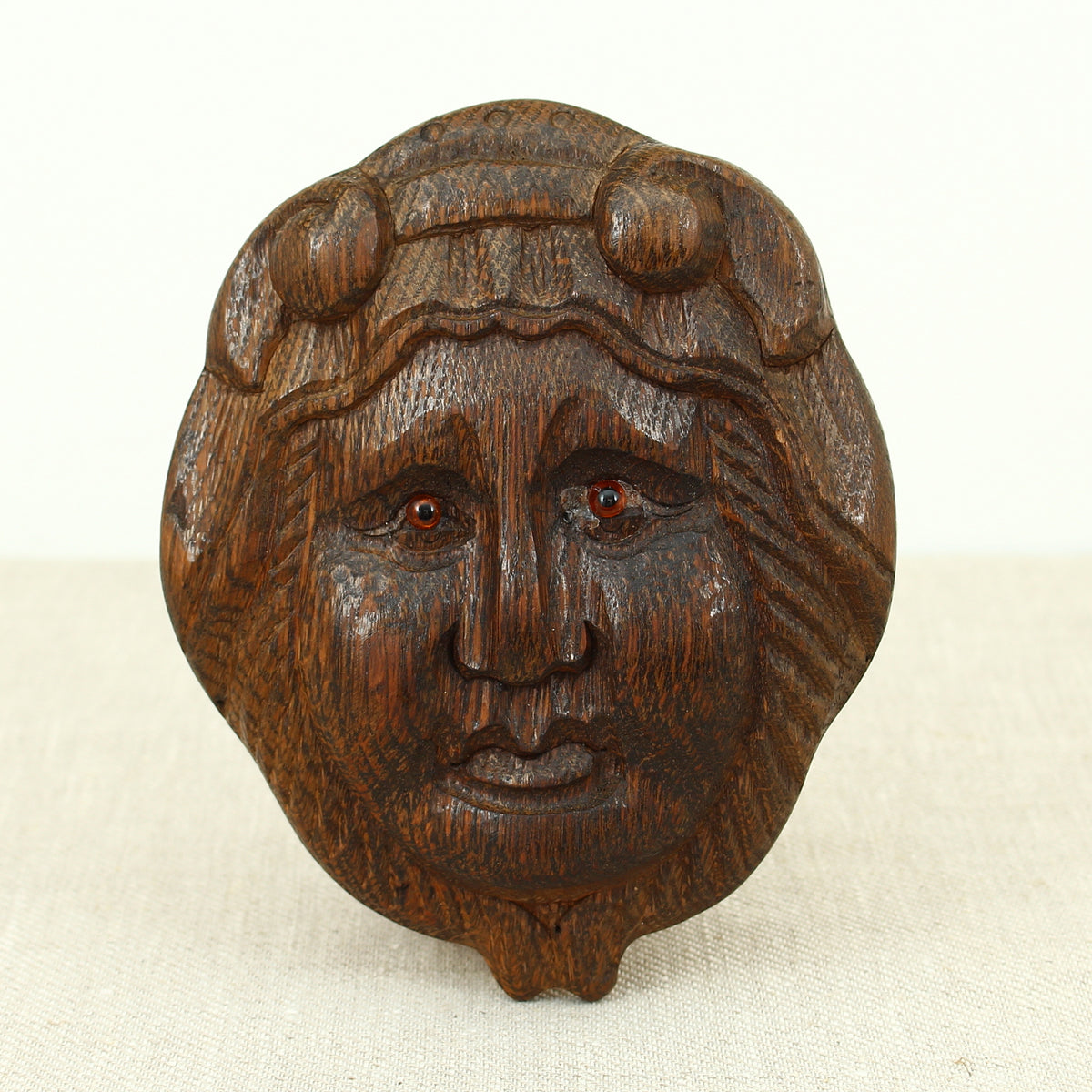 Treen - a carved oak fragment or furniture embellishment, carved as a mask with glass eyes