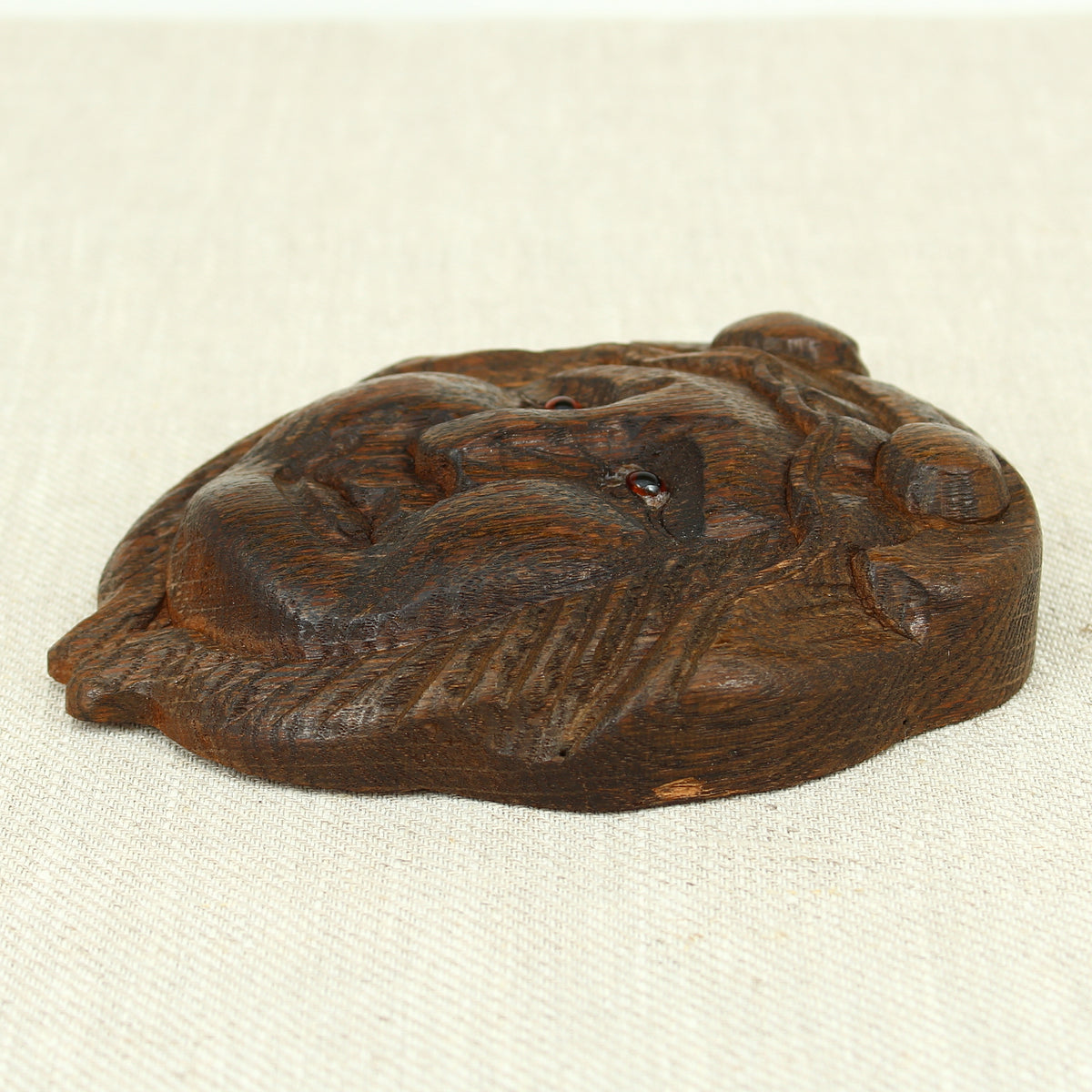 Treen - a carved oak fragment or furniture embellishment, carved as a mask with glass eyes
