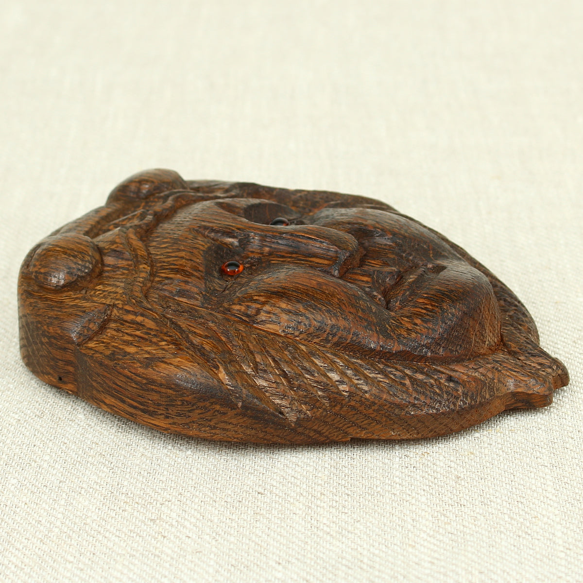 Treen - a carved oak fragment or furniture embellishment, carved as a mask with glass eyes