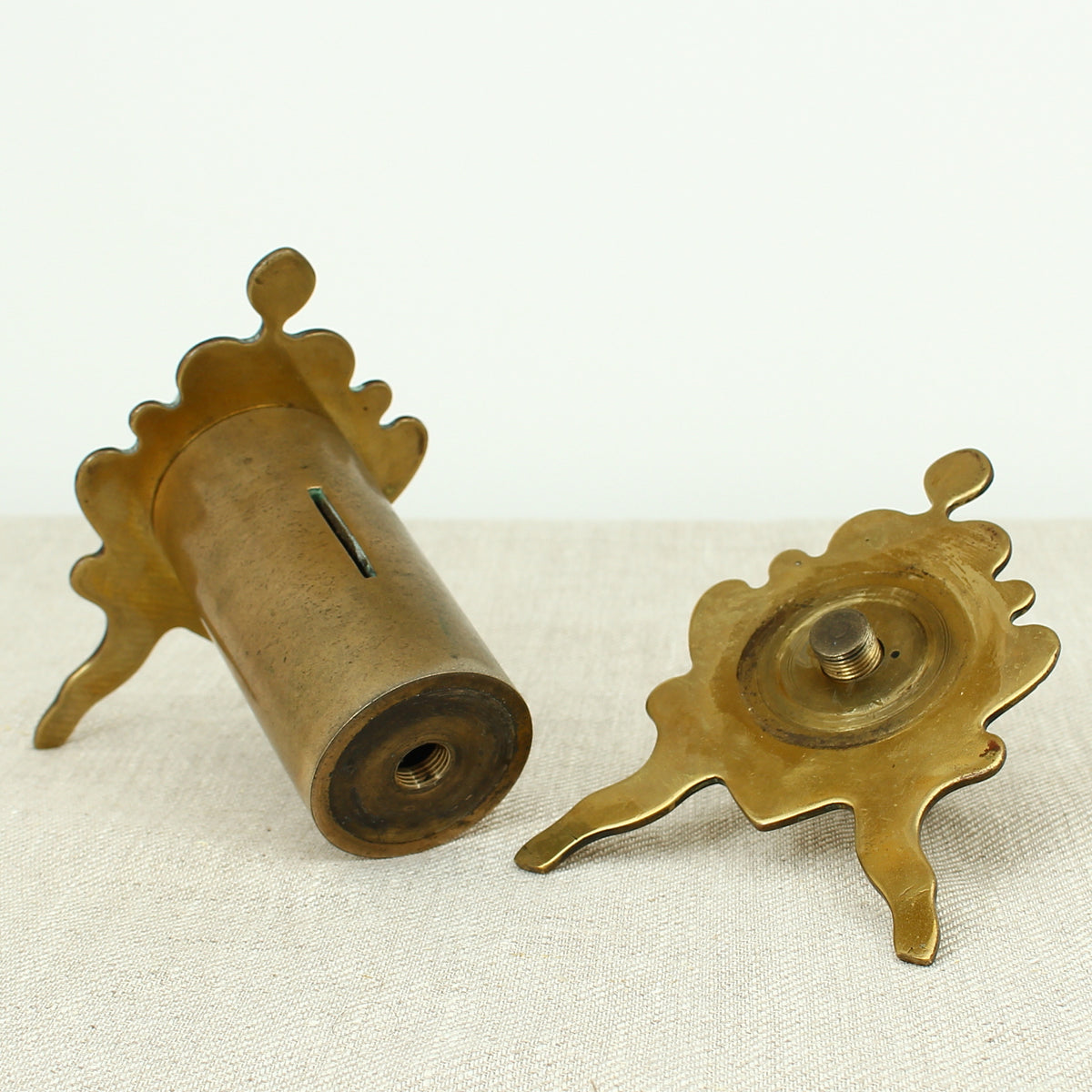 A late 19th century or early 20th century brass money box/bank, cylindrical central section with single money slot, shaped end pieces forming a combination pen rest, threaded finials to each end, 13.5cm high, 20cm wide