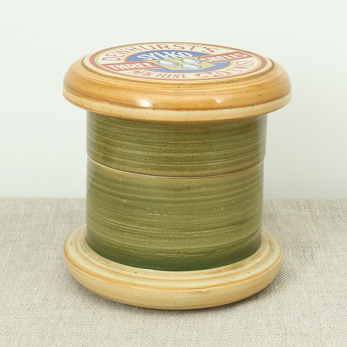 Advertising & Haberdashery Interest - a novelty ceramic jar, in the form of a faux oversized cotton reel, press close cover with printed design, 'DEWHURST'S SYLKO THREE SHELLS, MACHINE TWIST 40', finished in green, 15.5cm high