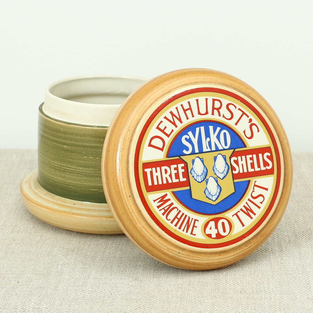 Advertising & Haberdashery Interest - a novelty ceramic jar, in the form of a faux oversized cotton reel, press close cover with printed design, 'DEWHURST'S SYLKO THREE SHELLS, MACHINE TWIST 40', finished in green, 15.5cm high